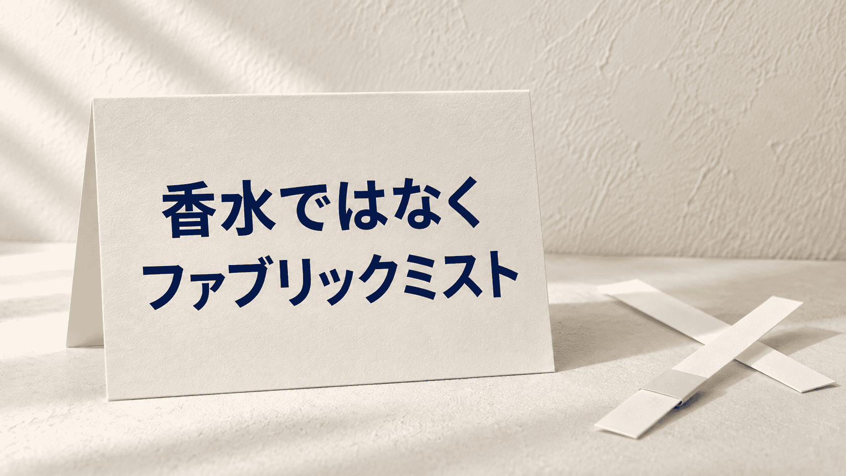 「香水ではなく ファブリックミスト」と印刷したカードと試香紙の静物イメージ